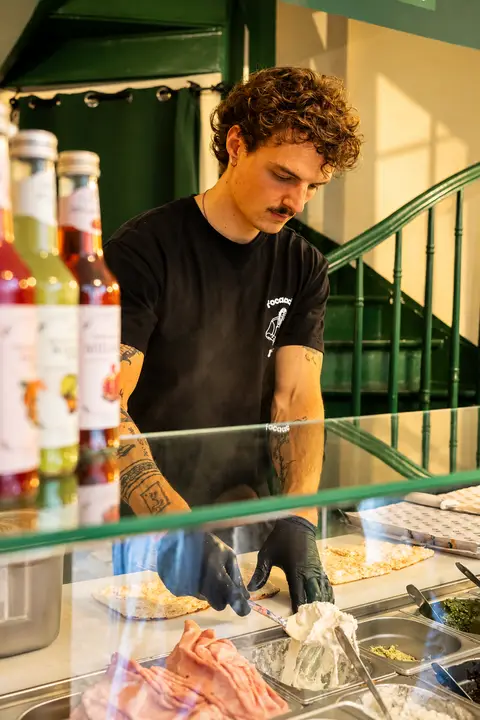 Un équipier Bart garnit une focaccia de stracciatella derrière le comptoir