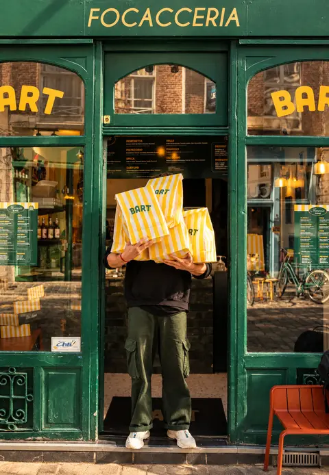 Façade verte de la focacceria Bart de Lille, un client chargé de sacs rayés Bart